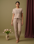 Woman wearing a beige t-shirt and pants with text, standing next to a vase of tulips on a green background.