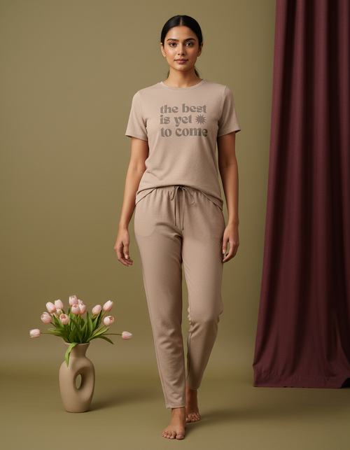 Woman wearing a beige t-shirt and pants with text, standing next to a vase of tulips on a green background.