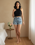 Woman wearing a black tank top and denim shorts standing in a bedroom.