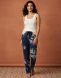 Woman wearing a white tank top and blue tie-dye pants against a brown background