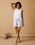 Woman wearing a white sleeveless top and light-colored shorts against a beige background
