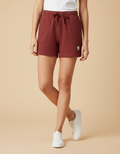 Person wearing maroon shorts and white sneakers on a beige background